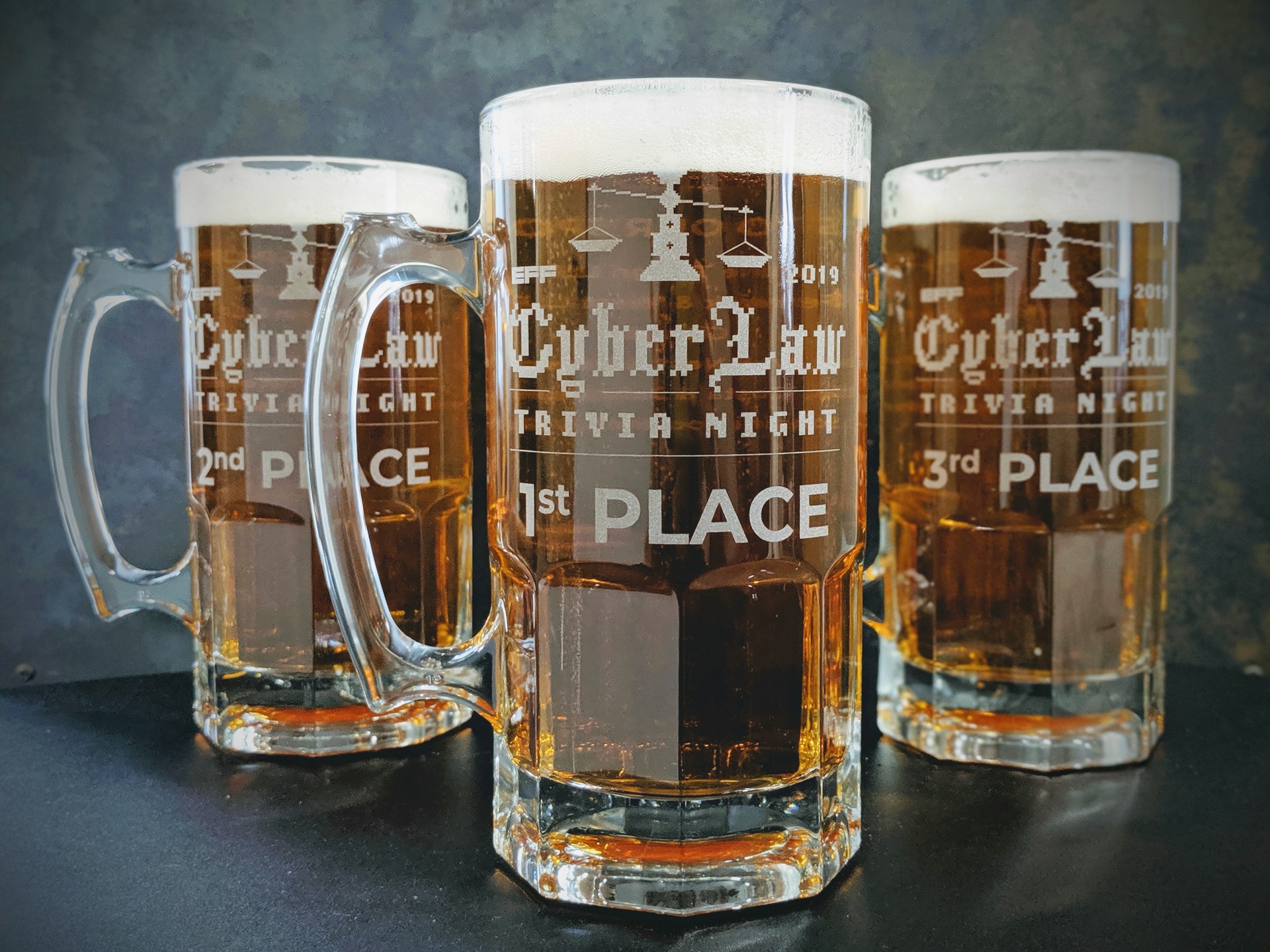 Photo of the coveted Cyberlaw Quiz Cups, which are actually large glass steins, filled with beer, with 1st place in the center, 2nd place to the left, and 3rd place to the right.