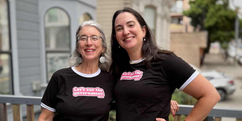Two people outside wearing black t-shirts with white trim that say "Let's sue the Government!"