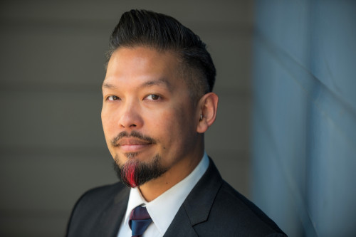 Person in a suit and tie in front of a blue background.